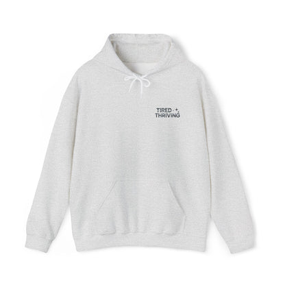 Minimal “Tired + Thriving” Embodied hoodie. Cozy fleece, unisex fit, durable chest graphic—everyday streetwear for busy days that still thrive.